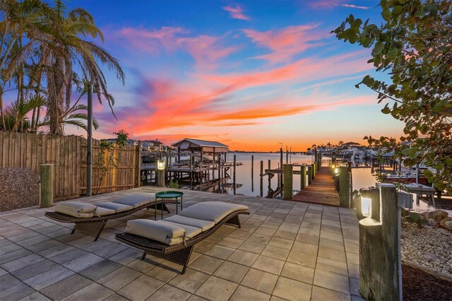 dock area with a water view, boat lift, fence, and a patio