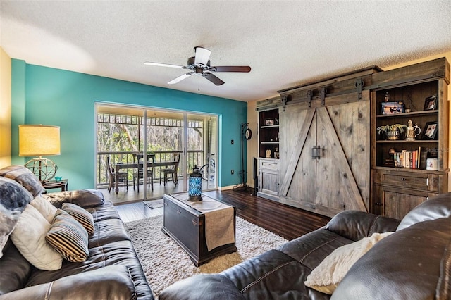 living area featuring a barn door, a ceiling fan, a textured ceiling, wood finished floors, and baseboards