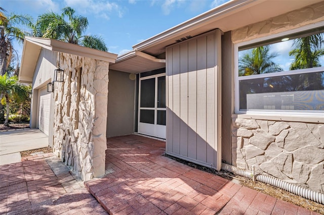 view of exterior entry with stone siding, an attached garage, and concrete driveway