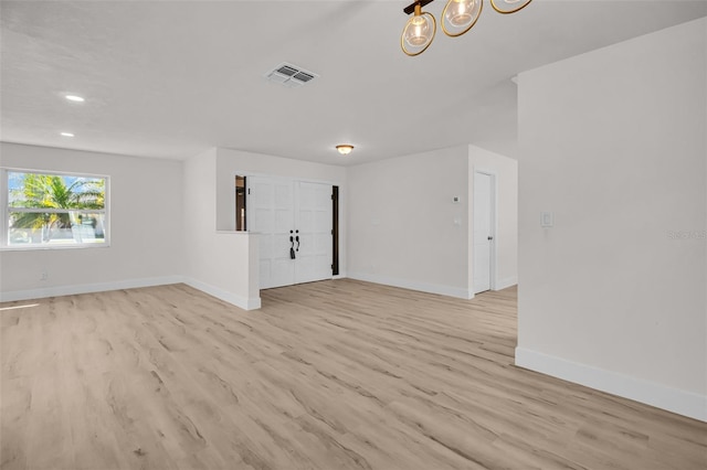 unfurnished room with light wood finished floors, an inviting chandelier, visible vents, and baseboards