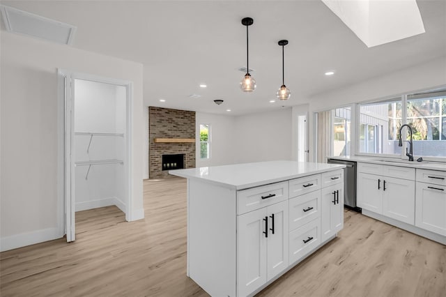 kitchen with stainless steel dishwasher, a brick fireplace, a sink, and light wood-style floors