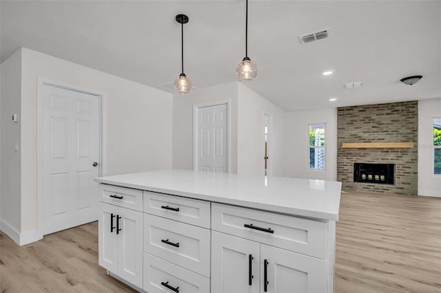 kitchen featuring a brick fireplace, visible vents, hanging light fixtures, light wood-style floors, and white cabinetry