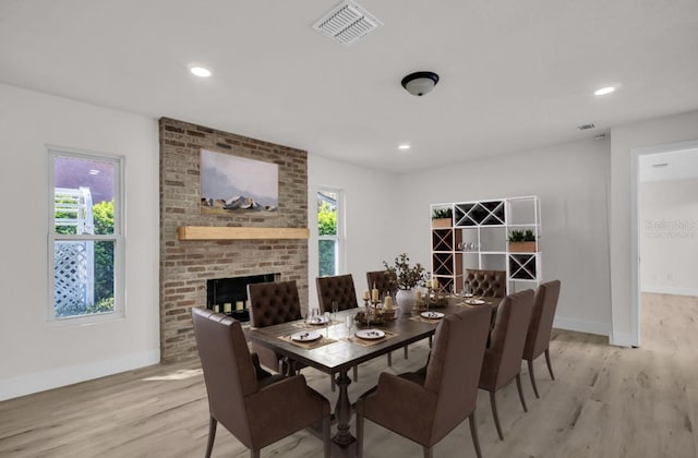 dining room featuring a brick fireplace, baseboards, visible vents, and light wood-style floors