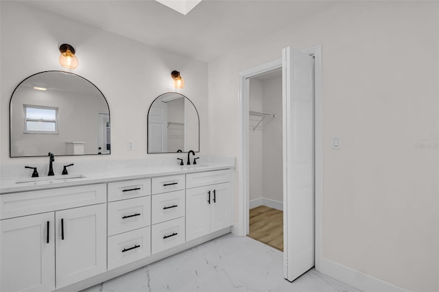 bathroom featuring marble finish floor, double vanity, a sink, and baseboards