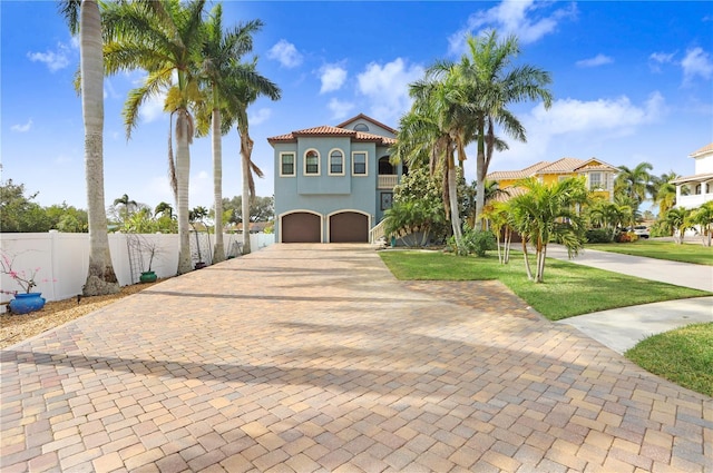 mediterranean / spanish home with a garage, stucco siding, fence, decorative driveway, and a front yard