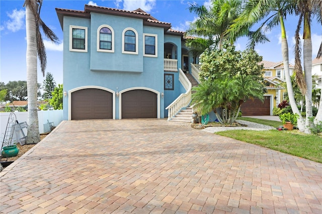 mediterranean / spanish home featuring decorative driveway, a tile roof, stucco siding, stairway, and a garage