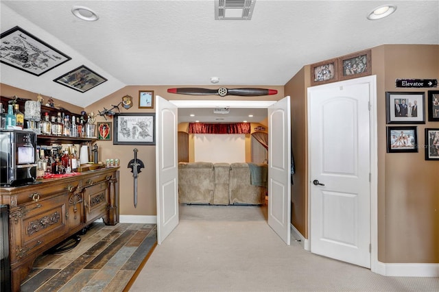 hall with lofted ceiling, a textured ceiling, visible vents, baseboards, and carpet