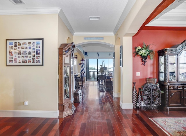 corridor with arched walkways, visible vents, dark wood-type flooring, ornamental molding, and baseboards