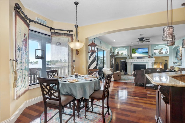 dining area featuring arched walkways, a fireplace, dark wood finished floors, and baseboards