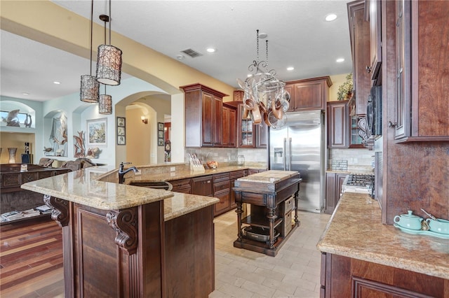 kitchen featuring visible vents, decorative backsplash, light stone counters, high end fridge, and a sink