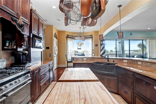 kitchen with hanging light fixtures, light stone countertops, stainless steel range with gas cooktop, black microwave, and a sink