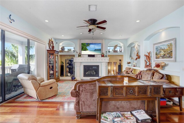 living room with ceiling fan, visible vents, wood finished floors, and a glass covered fireplace