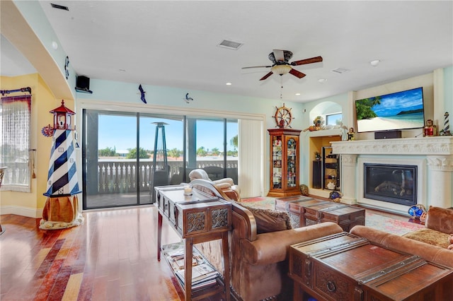 living room with ceiling fan, visible vents, wood finished floors, and a glass covered fireplace