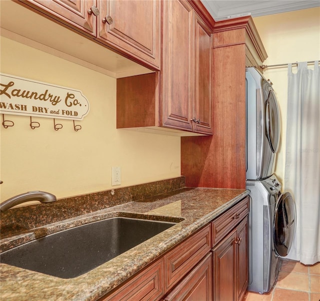 washroom featuring light tile patterned flooring, stacked washer and dryer, a sink, ornamental molding, and cabinet space