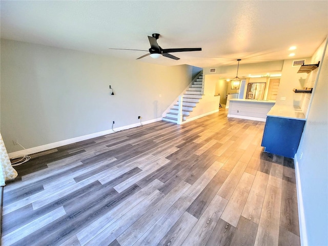 unfurnished living room featuring visible vents, stairway, baseboards, and wood finished floors