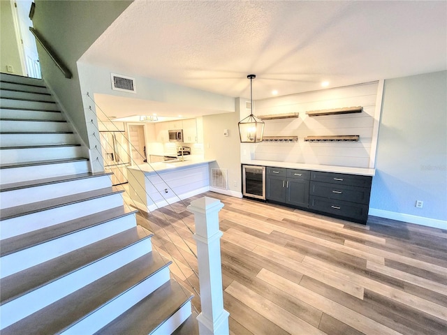 bar with wine cooler, visible vents, stainless steel microwave, light wood-type flooring, and stairs