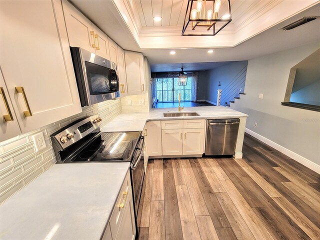 kitchen with visible vents, appliances with stainless steel finishes, a peninsula, a tray ceiling, and a sink