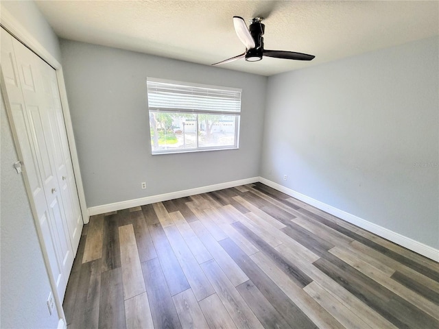 unfurnished bedroom featuring a textured ceiling, a closet, baseboards, and wood finished floors