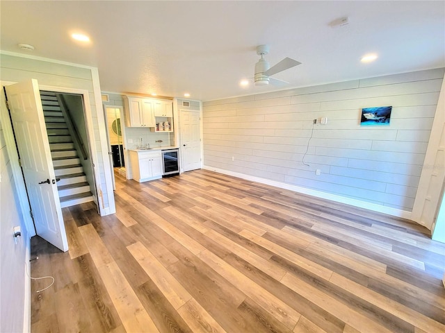 unfurnished living room with wine cooler, light wood finished floors, stairway, a ceiling fan, and a sink