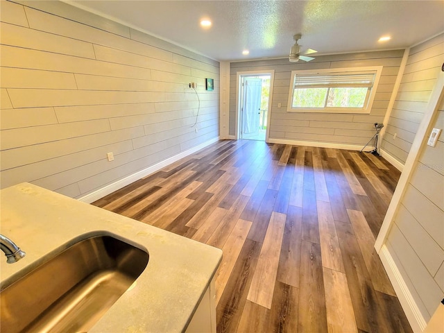 unfurnished living room featuring ceiling fan, recessed lighting, a sink, wood finished floors, and baseboards