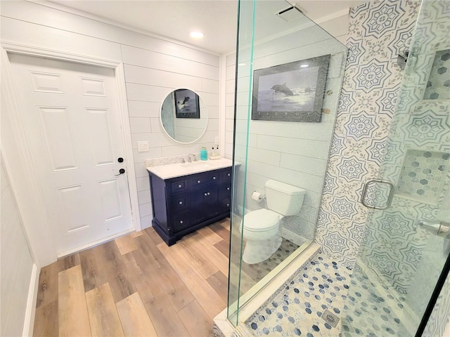 bathroom featuring tile walls, toilet, a stall shower, vanity, and wood finished floors