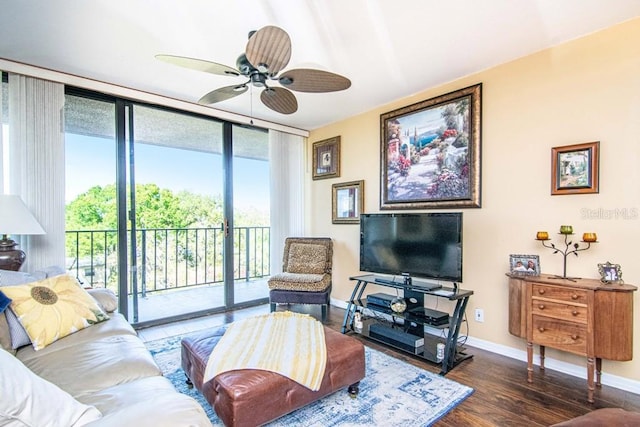 living room featuring a ceiling fan, baseboards, a wall of windows, and wood finished floors