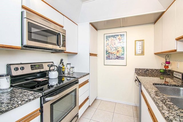 kitchen with light tile patterned floors, appliances with stainless steel finishes, white cabinets, and dark stone counters