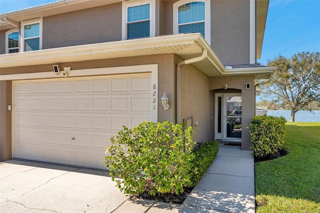 view of exterior entry with a water view, an attached garage, and stucco siding