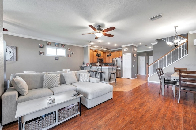 living room with crown molding, stairs, visible vents, and wood finished floors