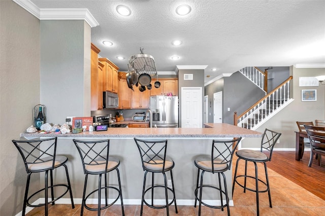 kitchen featuring a peninsula, appliances with stainless steel finishes, light countertops, and crown molding