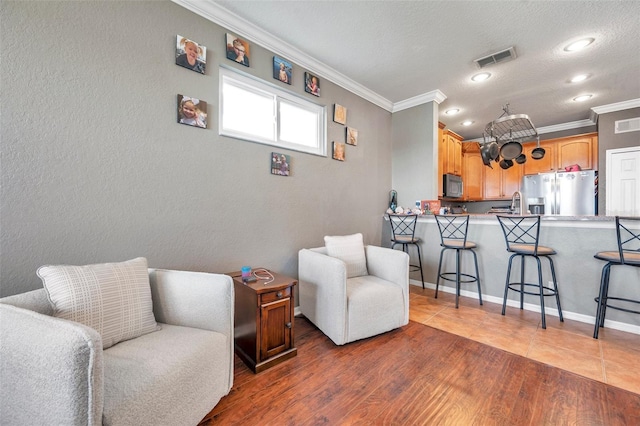 living area with a textured ceiling, a textured wall, wood finished floors, visible vents, and crown molding