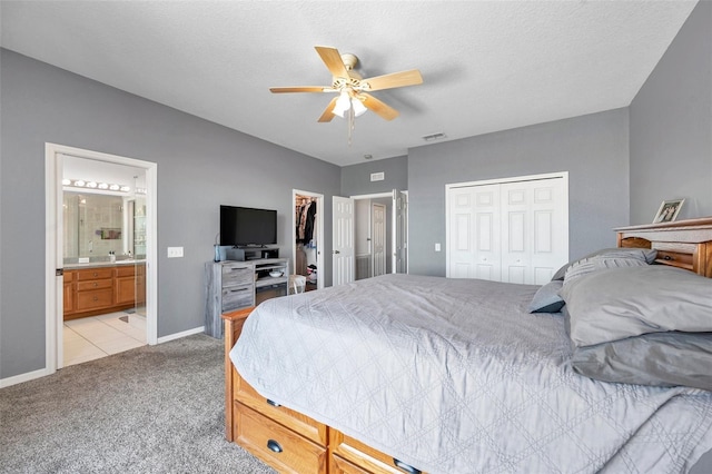 bedroom with light colored carpet, visible vents, a ceiling fan, ensuite bath, and baseboards