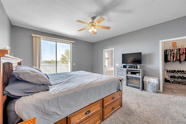 carpeted bedroom featuring ensuite bathroom, a textured ceiling, ceiling fan, access to outside, and a walk in closet