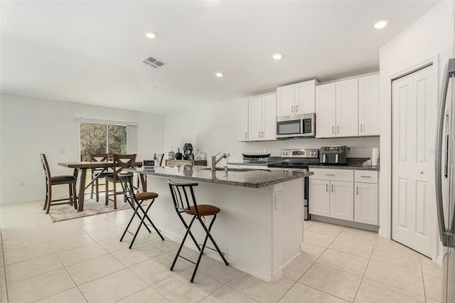 kitchen with visible vents, appliances with stainless steel finishes, a sink, dark stone countertops, and a kitchen bar