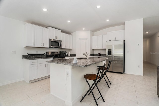 kitchen with light tile patterned floors, stainless steel appliances, white cabinets, a kitchen breakfast bar, and dark stone countertops