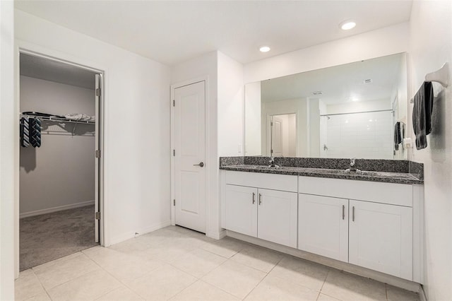 bathroom featuring a sink, tile patterned floors, double vanity, a stall shower, and a walk in closet