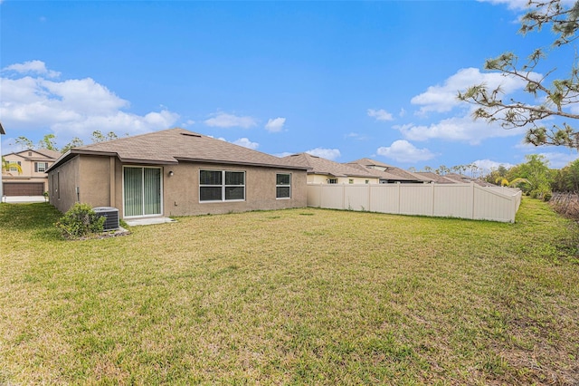 rear view of property with central AC unit, a lawn, fence, and stucco siding