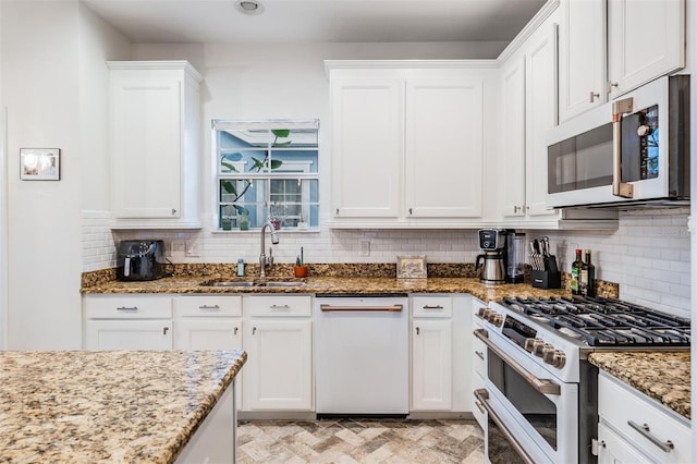 kitchen featuring white appliances, light stone counters, a sink, white cabinetry, and backsplash