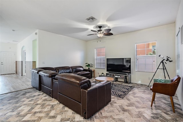 living room featuring brick floor, arched walkways, visible vents, ceiling fan, and baseboards