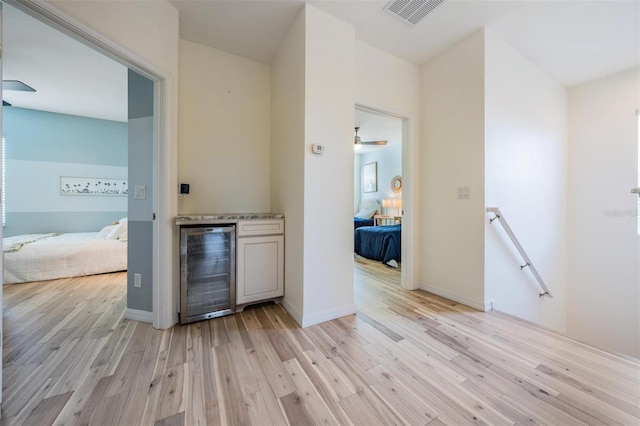 hall with light wood-style floors, beverage cooler, visible vents, and an upstairs landing