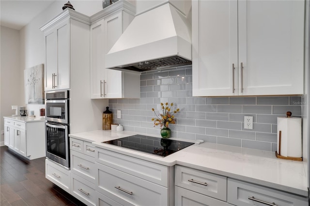 kitchen featuring dark wood finished floors, custom exhaust hood, double oven, white cabinets, and black electric cooktop