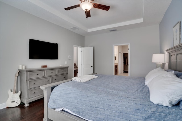 bedroom with dark wood-style floors, visible vents, a tray ceiling, and ceiling fan