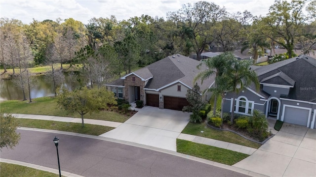 view of front facade with a garage, concrete driveway, stone siding, a water view, and a front yard