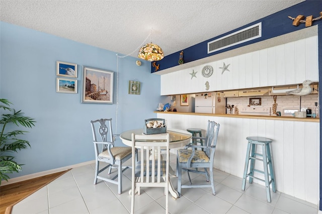 tiled dining space with baseboards, visible vents, and a textured ceiling