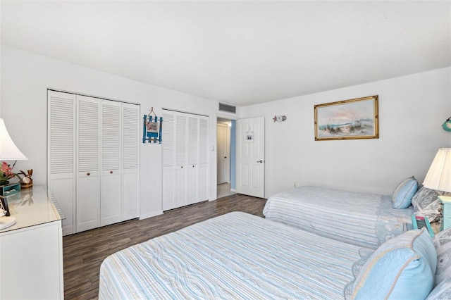 bedroom featuring dark wood finished floors, visible vents, and two closets