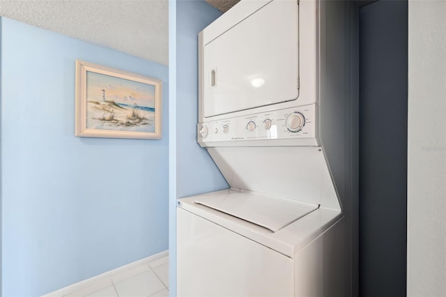 laundry room featuring laundry area, stacked washer / dryer, light tile patterned flooring, and a textured ceiling