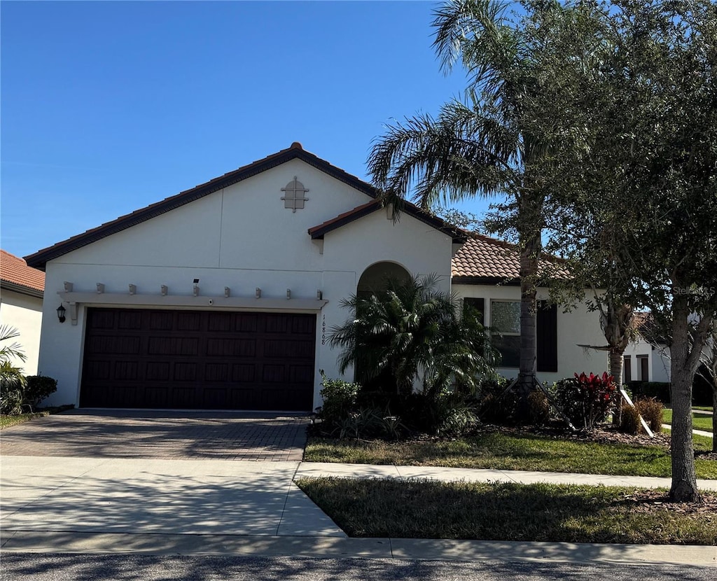 mediterranean / spanish-style home with a garage, driveway, a tiled roof, and stucco siding