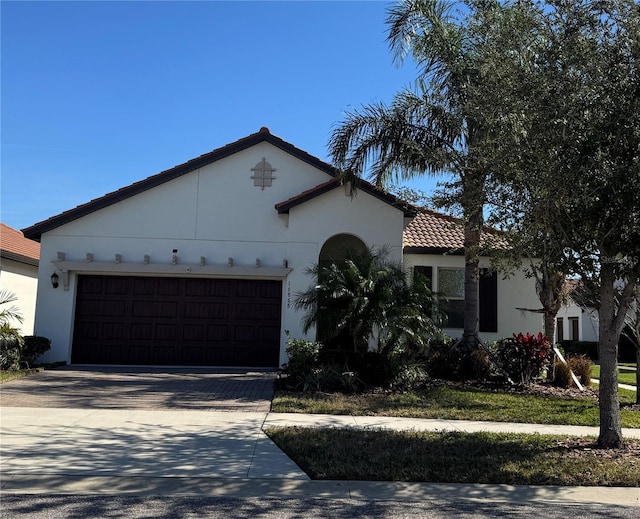 mediterranean / spanish-style home with a garage, driveway, a tiled roof, and stucco siding