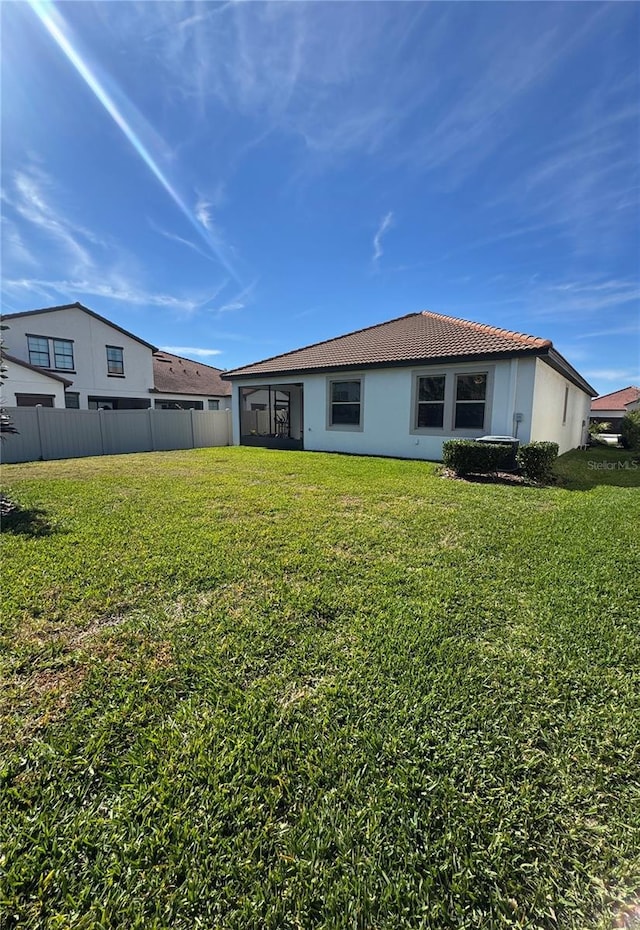 back of property featuring a tile roof, stucco siding, fence, and a lawn