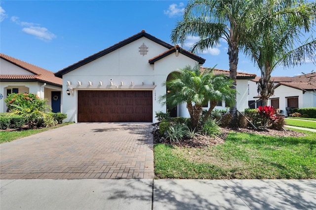 mediterranean / spanish house with a tiled roof, decorative driveway, a garage, and stucco siding